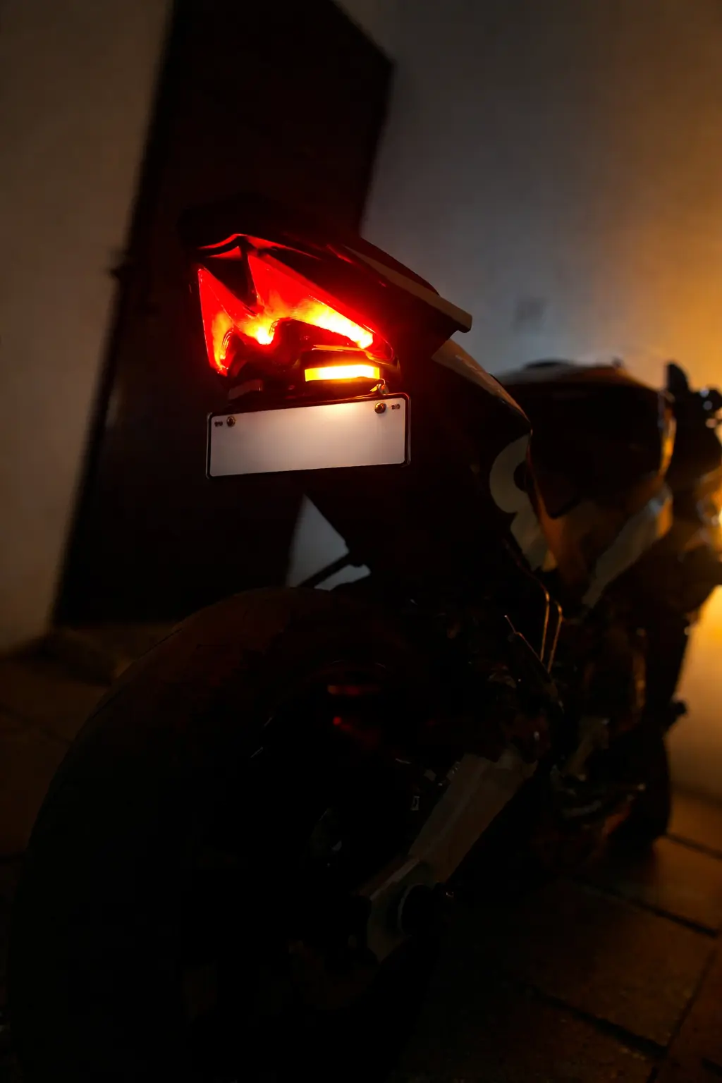 Low-light rear view of a sport motorcycle with Split LED indicators and number plate light illuminated